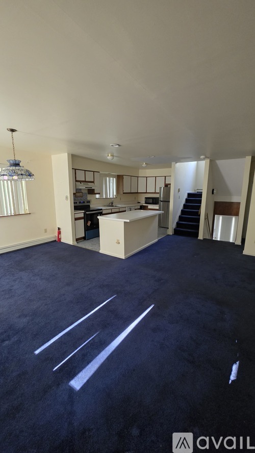 A spacious room with a kitchen area and stairs in the background.