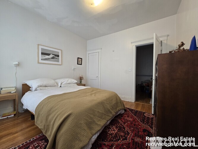 A bedroom with a bed covered in a blanket and a painting on the wall.