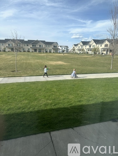 Two people are walking in a grassy area in front of a row of houses.