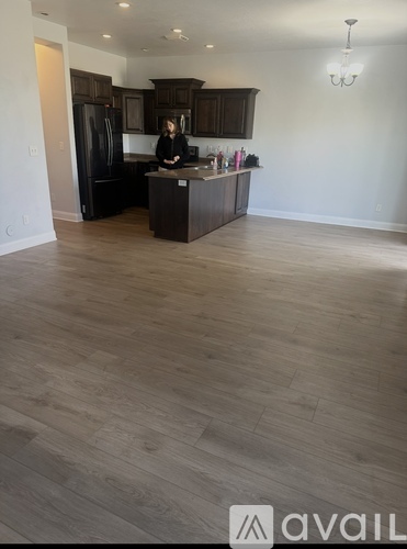 A woman is standing in a kitchen with wooden floors and dark cabinets.