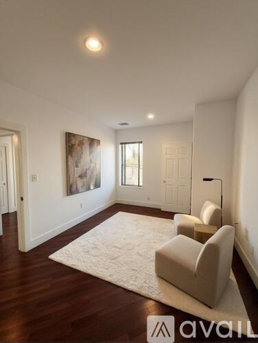 A living room with a rug, a chair and a painting on the wall.