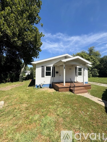 A small white house with a porch and a tree in front.