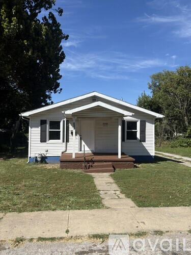 A small white house with a porch and a tree in front.