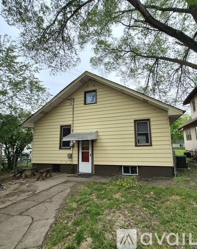 A yellow house with a red door and a window is surrounded by trees.