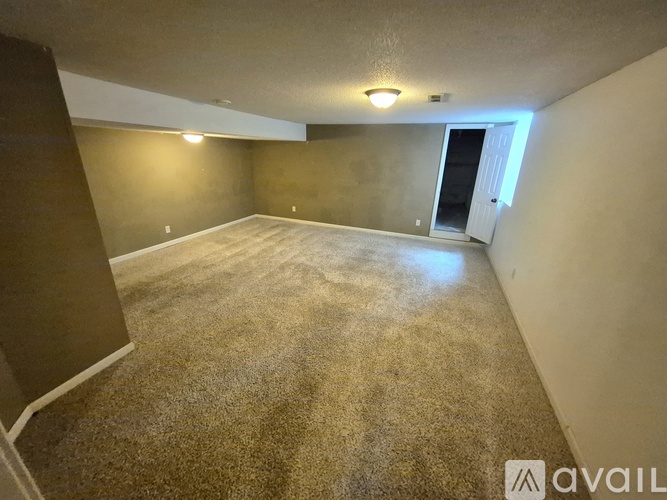 A room with carpeted floor and a door on the right side.