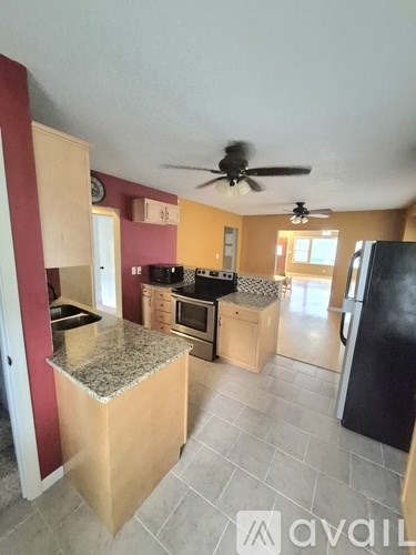 A kitchen with a black refrigerator and a ceiling fan.