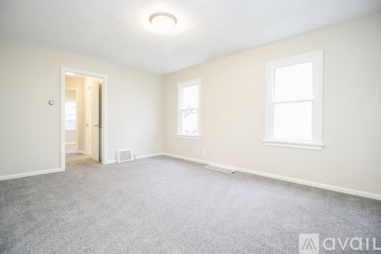 A room with a carpeted floor, two windows, and a door leading to another room.
