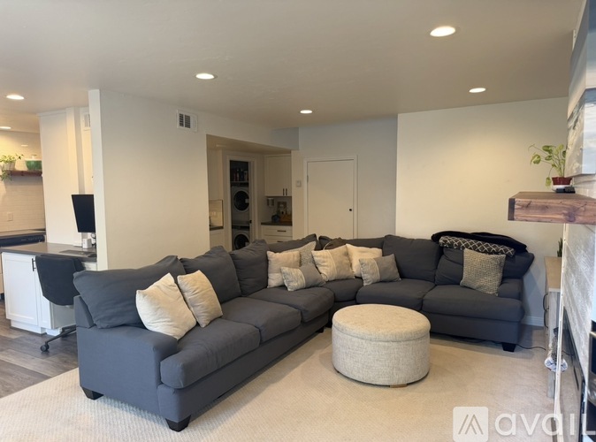 A grey sectional sofa with a round ottoman in front of it.