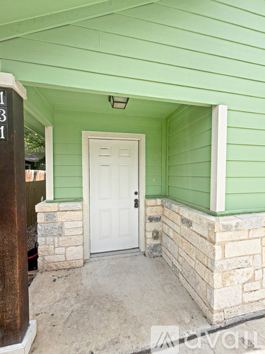 A green house with a white door and a brown sign on the left.