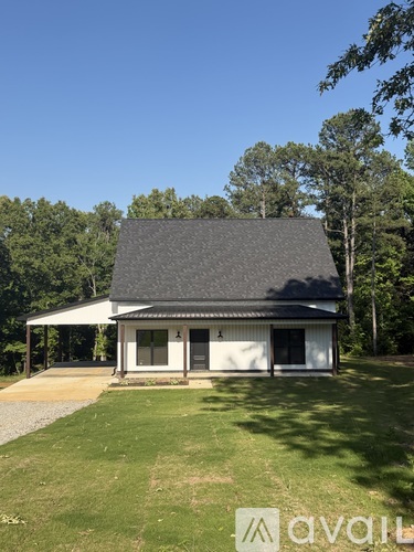 A house with a grey roof and white walls is surrounded by greenery.