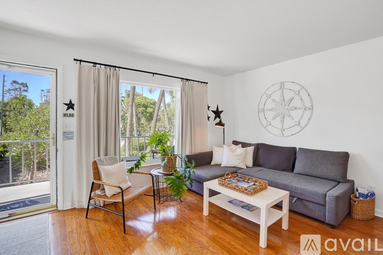 A living room with a grey couch, a white coffee table, and a large window with a view of trees.