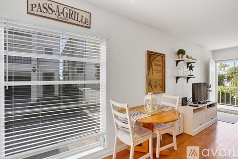 A living room with a dining table and chairs, a television, and a window with blinds.