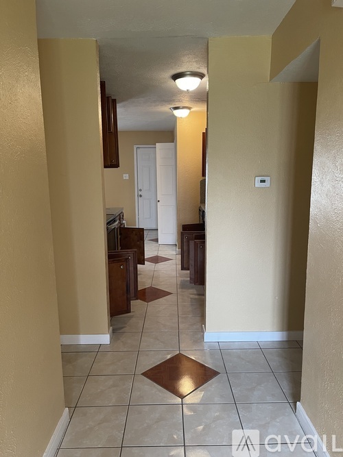 A hallway with a brown square tile floor and white walls.