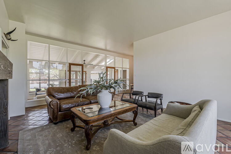 A living room with a brown leather couch, a wooden coffee table, and a large window.