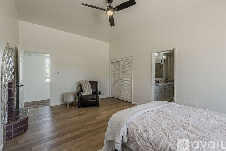 A bedroom with a bed, chair, and a fan.