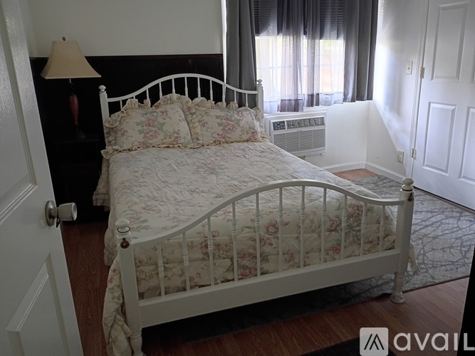 A white bed with a floral comforter is in a room with a lamp and a window.