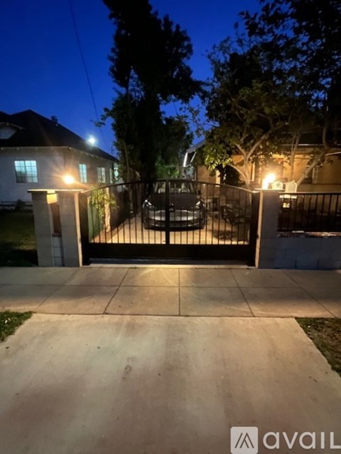 A driveway leads to a house with a gate and lights on.