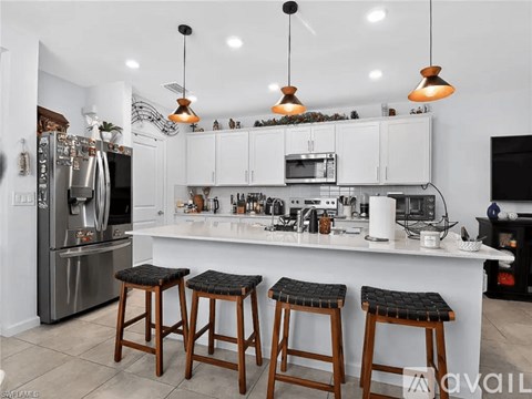 A kitchen with white cabinets and a white countertop with two bar stools.