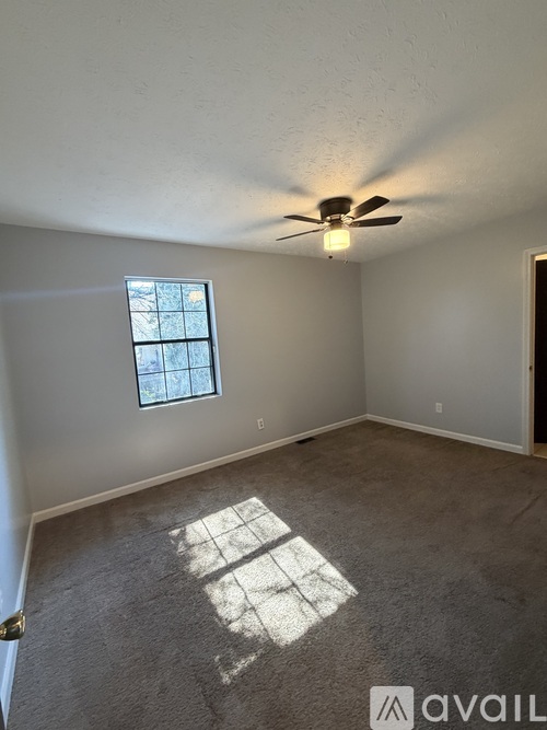 A room with a ceiling fan and a window letting in sunlight.