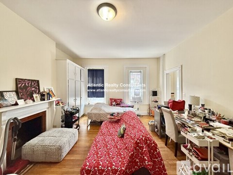 A room with a red bedspread and a fireplace.