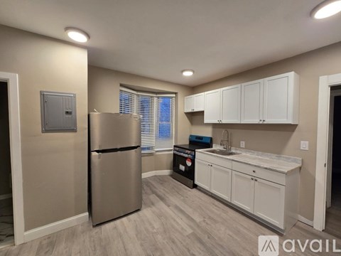 A kitchen with a stainless steel refrigerator, white cabinets, and a wooden floor.