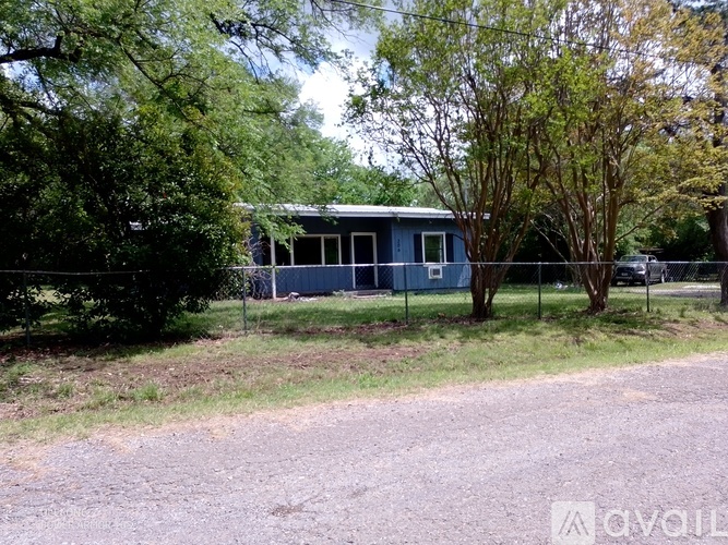 A blue house with a metal roof is surrounded by trees and grass.