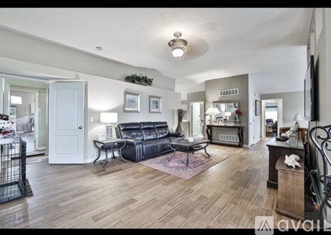 A living room with a black leather couch and a wooden floor.