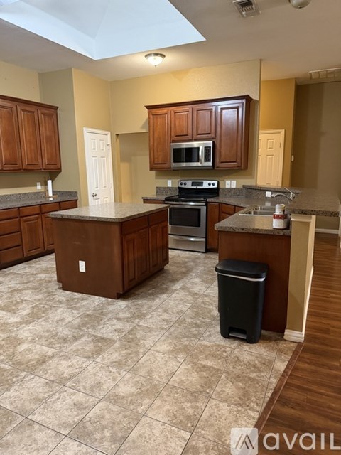A kitchen with brown cabinets and a black trash can.