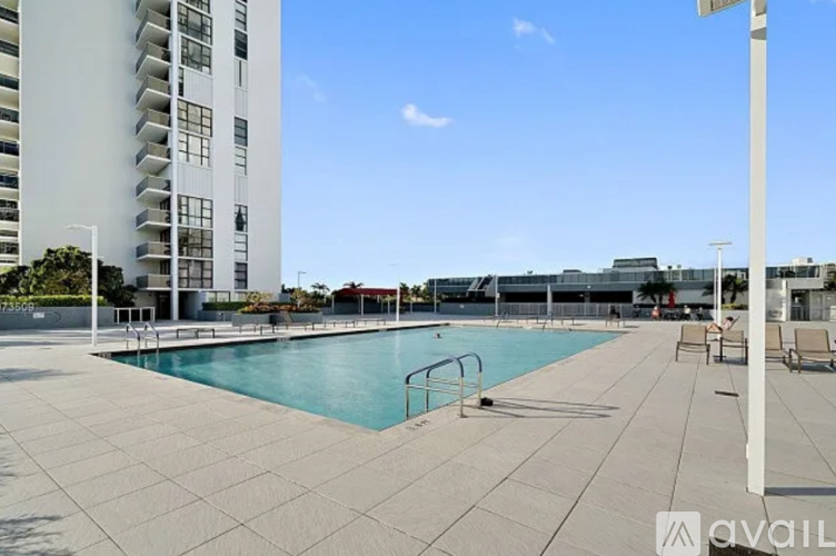 A large outdoor swimming pool surrounded by a tiled patio and a tall white building.