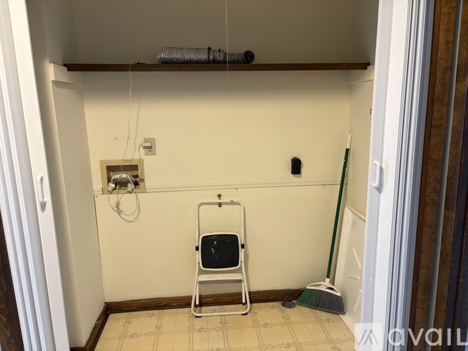 A white chair is in a corner of a room with a broom on the floor.
