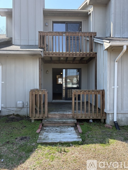 A wooden deck leads to a doorway in a white building.