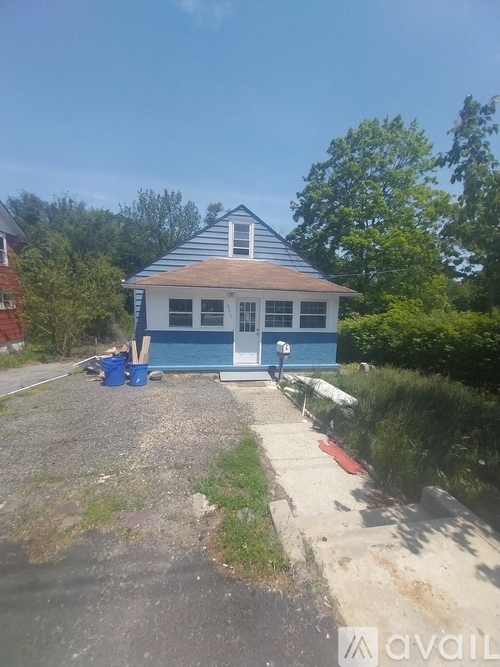 A blue house with a white roof and a red door is surrounded by greenery.