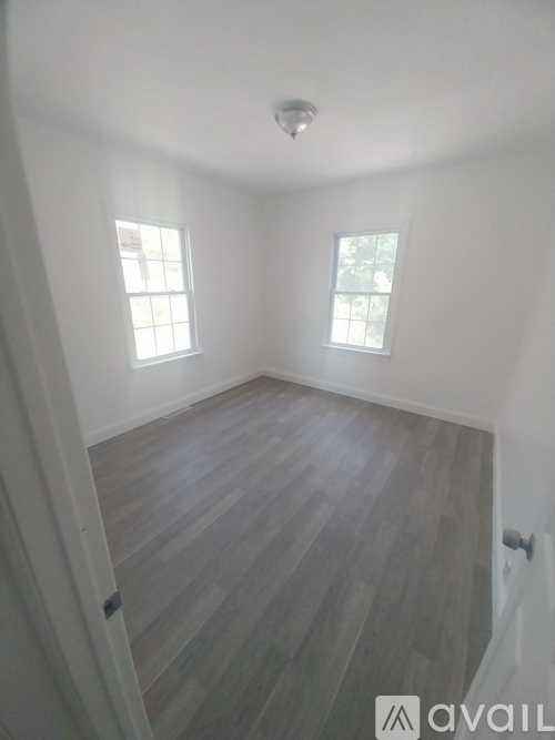 A room with wooden flooring and two windows.