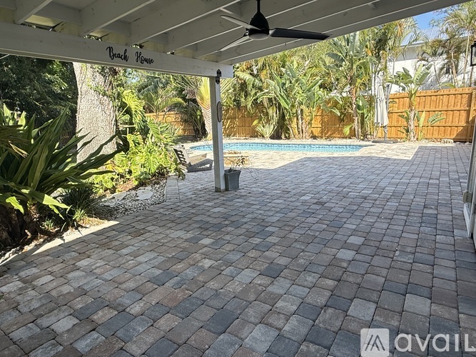 A patio area with a brick pattern floor and a pool in the background.