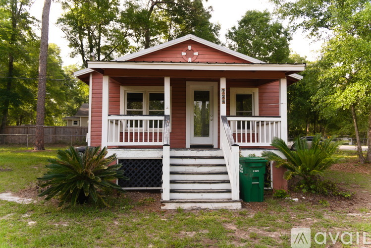 A small red house with a white porch and a green trash can in front.