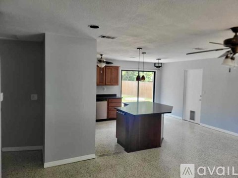 A spacious living room with a kitchen area in the background.