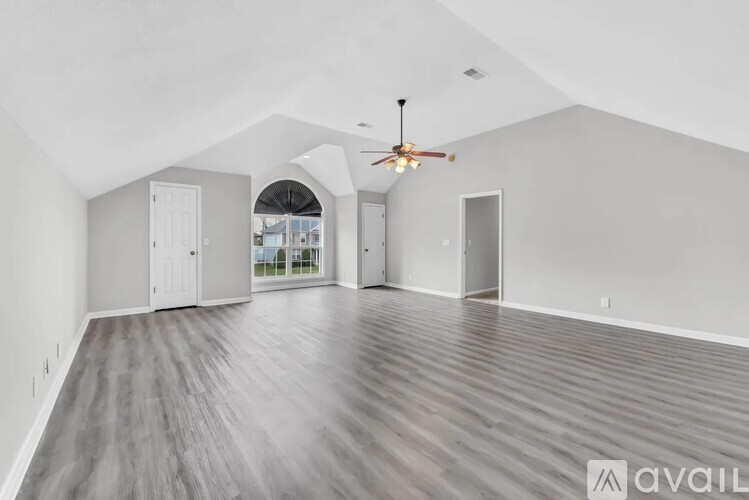 A spacious room with a ceiling fan and light, and a large window with a view of the outdoors.