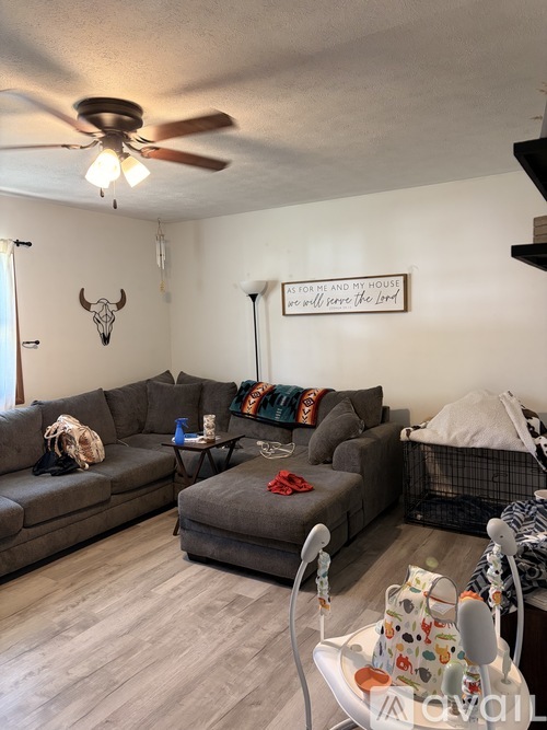 A living room with a grey couch, a black chair, and a white ceiling fan.