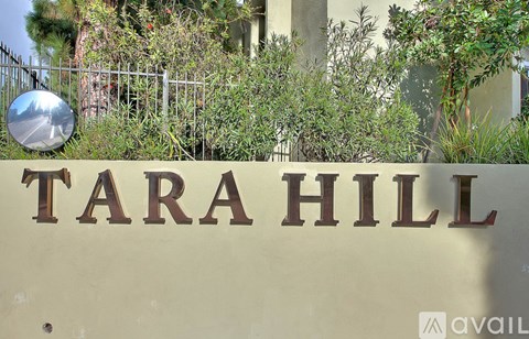 A sign that says TARA HILL in front of a fence and plants.