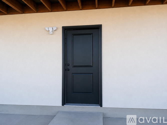 A black door with a small window in the middle is set in a white wall.