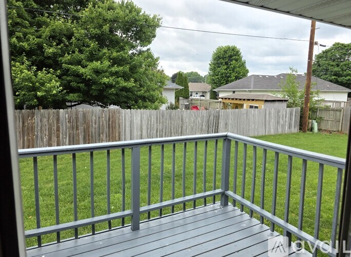 A deck with a grey railing and a view of a backyard with a fence and trees.