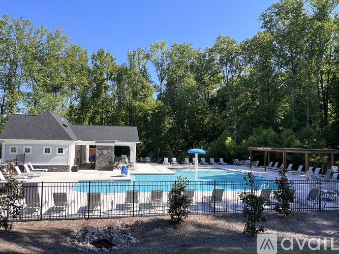 A pool surrounded by chairs and trees with a house in the background.