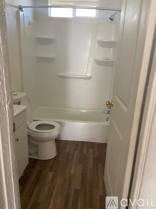 A white bathroom with wood flooring and a toilet.