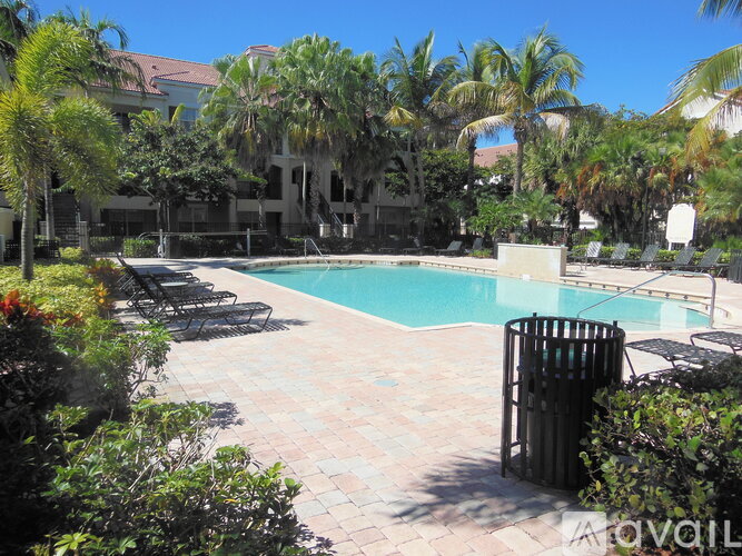 A pool surrounded by palm trees and a building in the background.