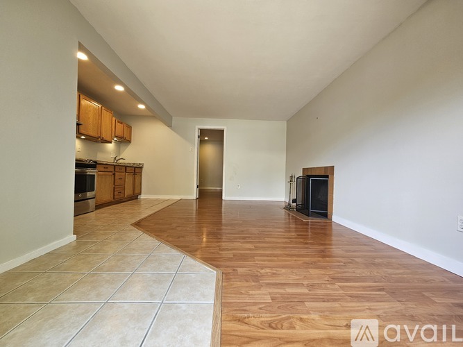 A spacious room with wooden flooring and a kitchen area in the background.