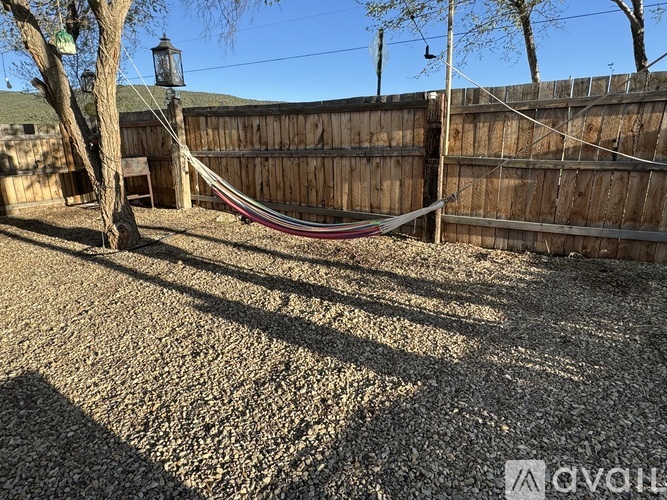 A hammock is strung between two trees in a backyard.
