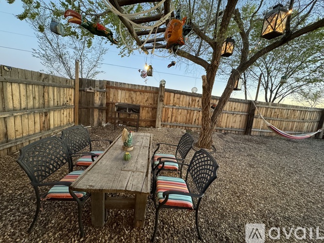 A backyard with a wooden table and chairs under a tree.