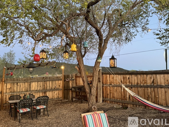 A backyard with a tree, chairs, and a hammock.