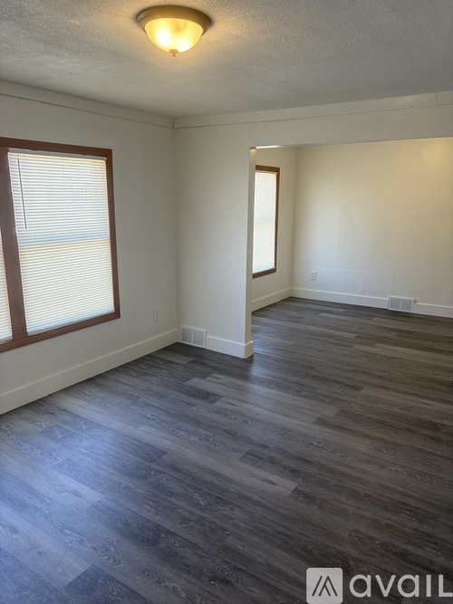 A room with wooden flooring and two windows.