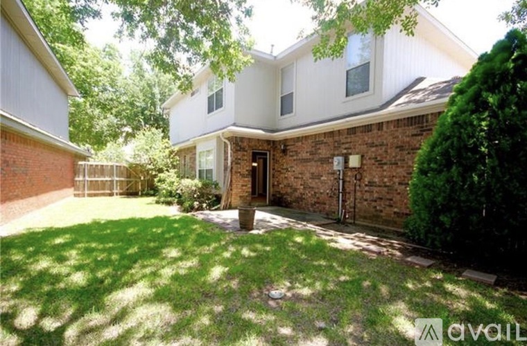 A house with a white exterior and a brown door is surrounded by a green lawn.